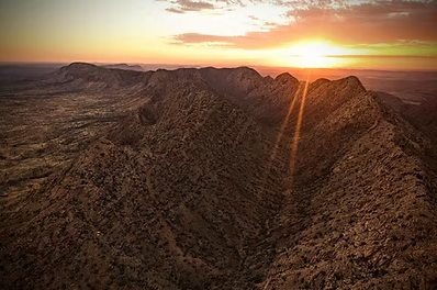 View from a helicopter cockpit: islands dot a blue lake at sunset.