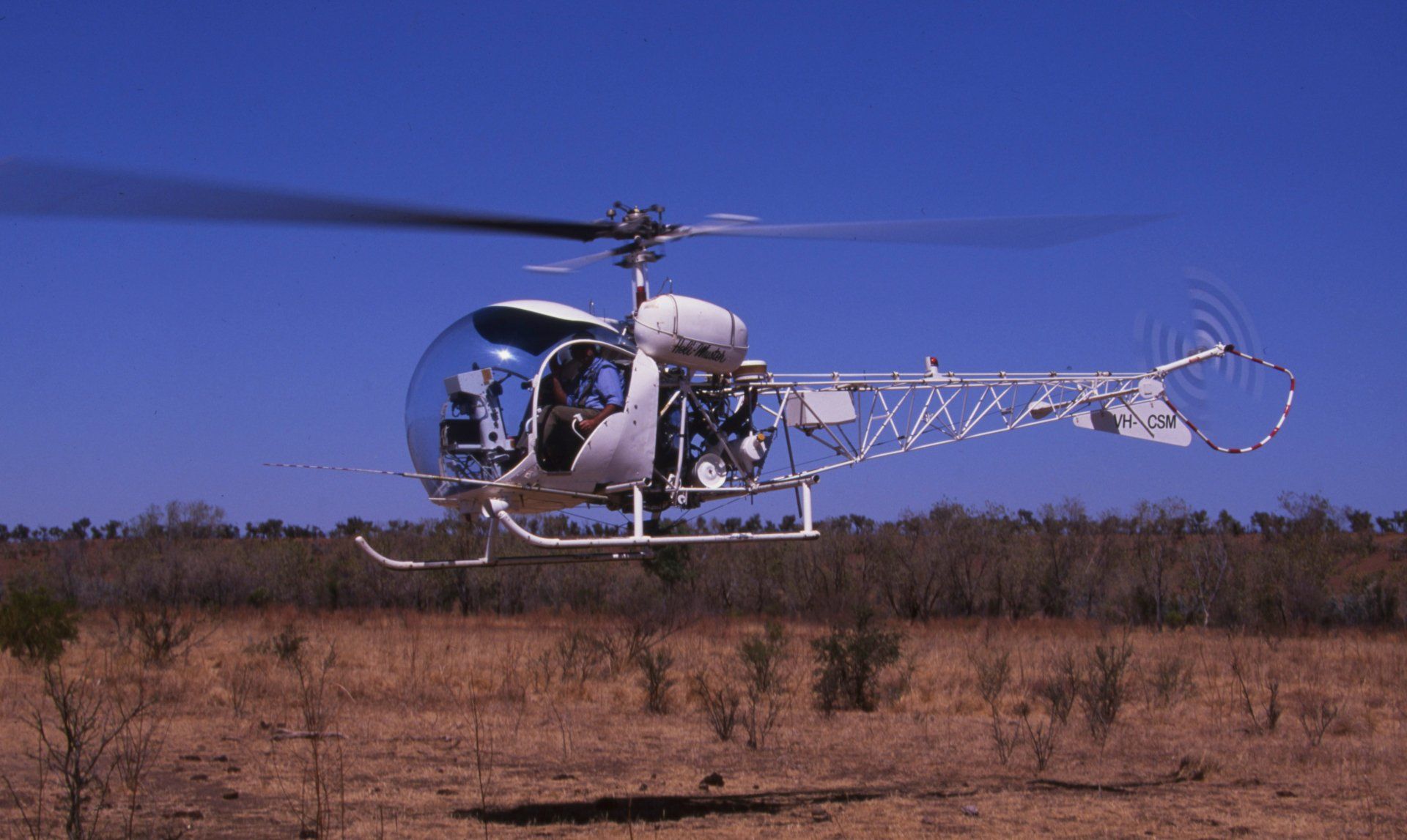 White helicopter in flight over dry landscape, clear blue sky.