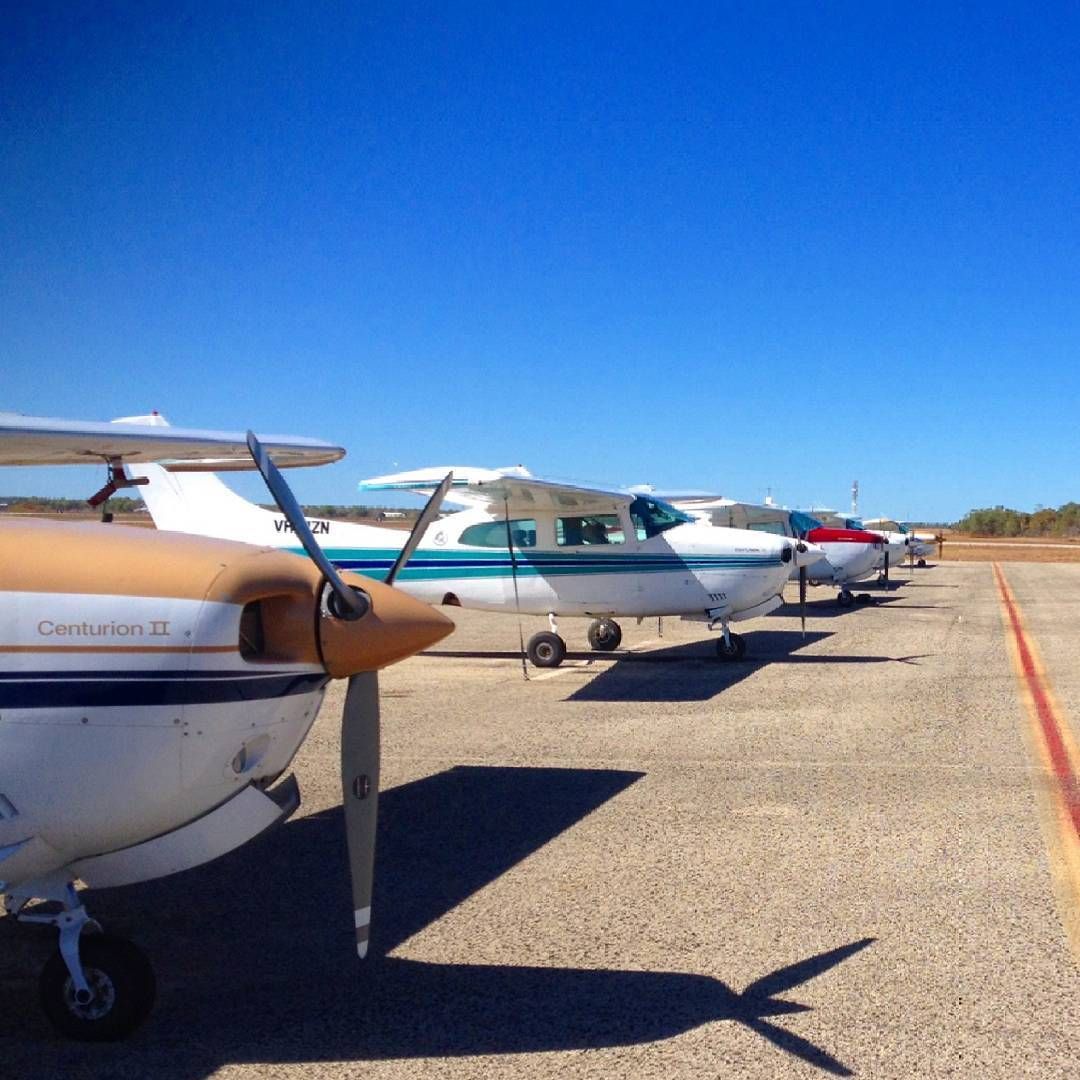 Small airplanes parked on a runway under a bright blue sky.