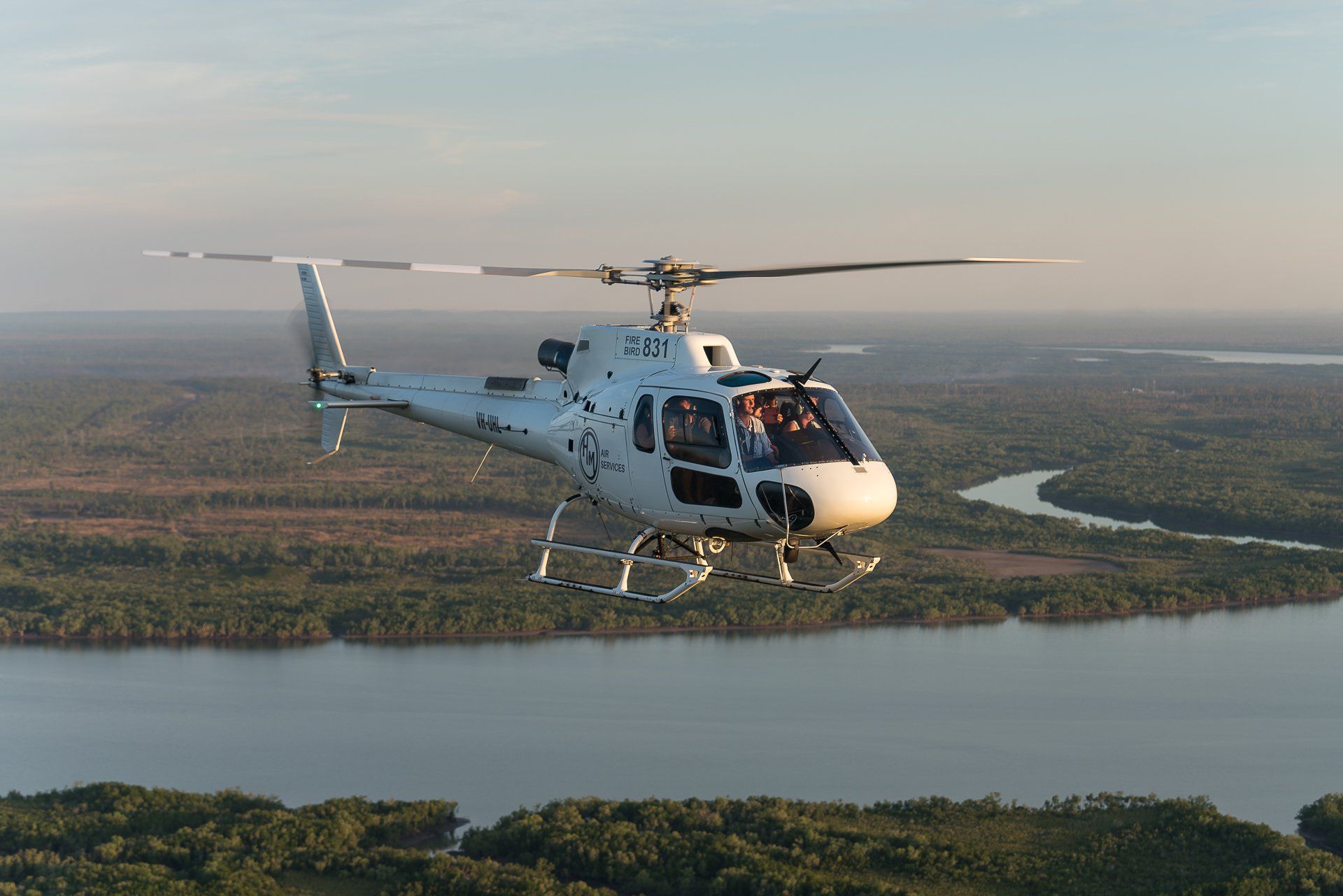 Helicopter flying over a river and forested landscape.