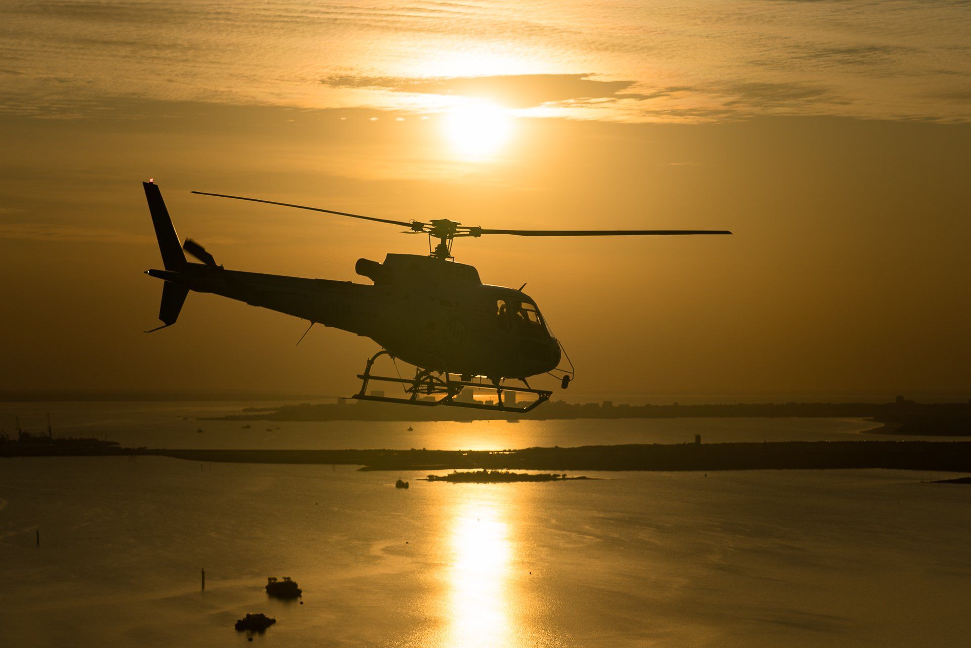 Helicopter silhouetted against a setting sun over water.