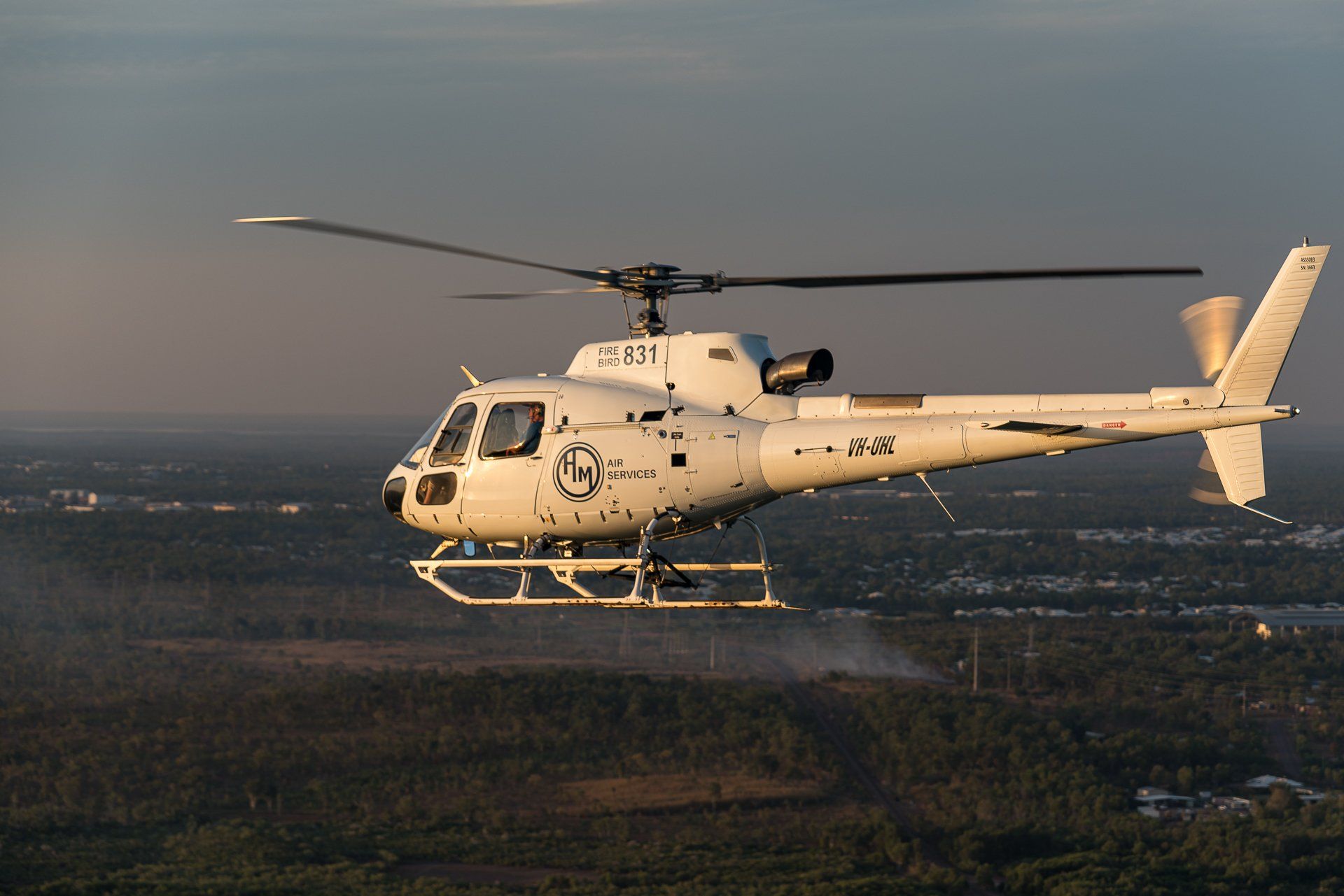 White helicopter flying over a forest.