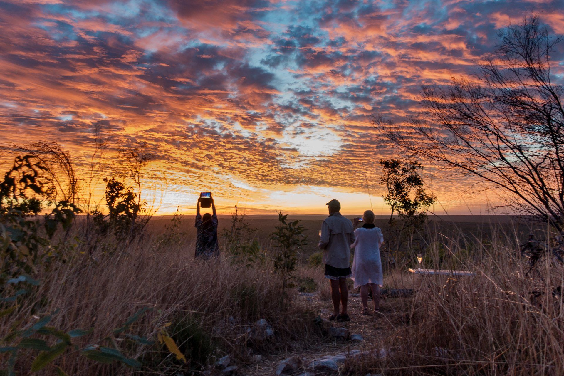 People watching sunset over a distant horizon, silhouetted in front of colorful orange and pink clouds.