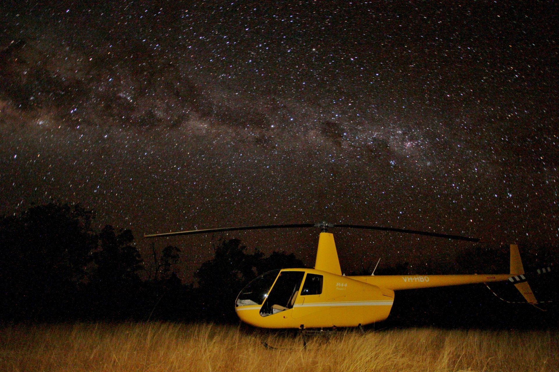 Yellow helicopter parked on the ground under a starry night sky; Milky Way visible.