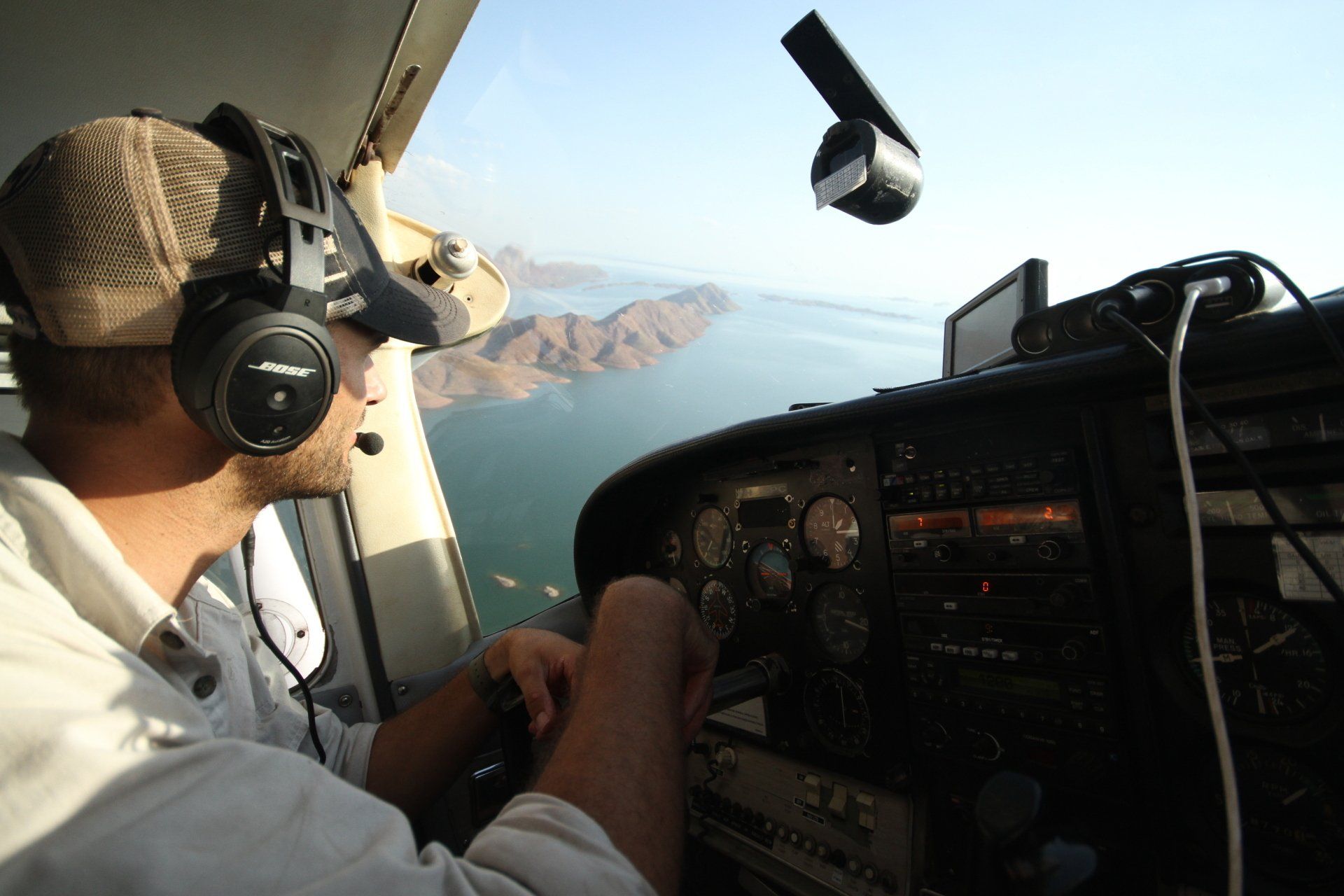 Pilot in cockpit looking out over water and mountains.