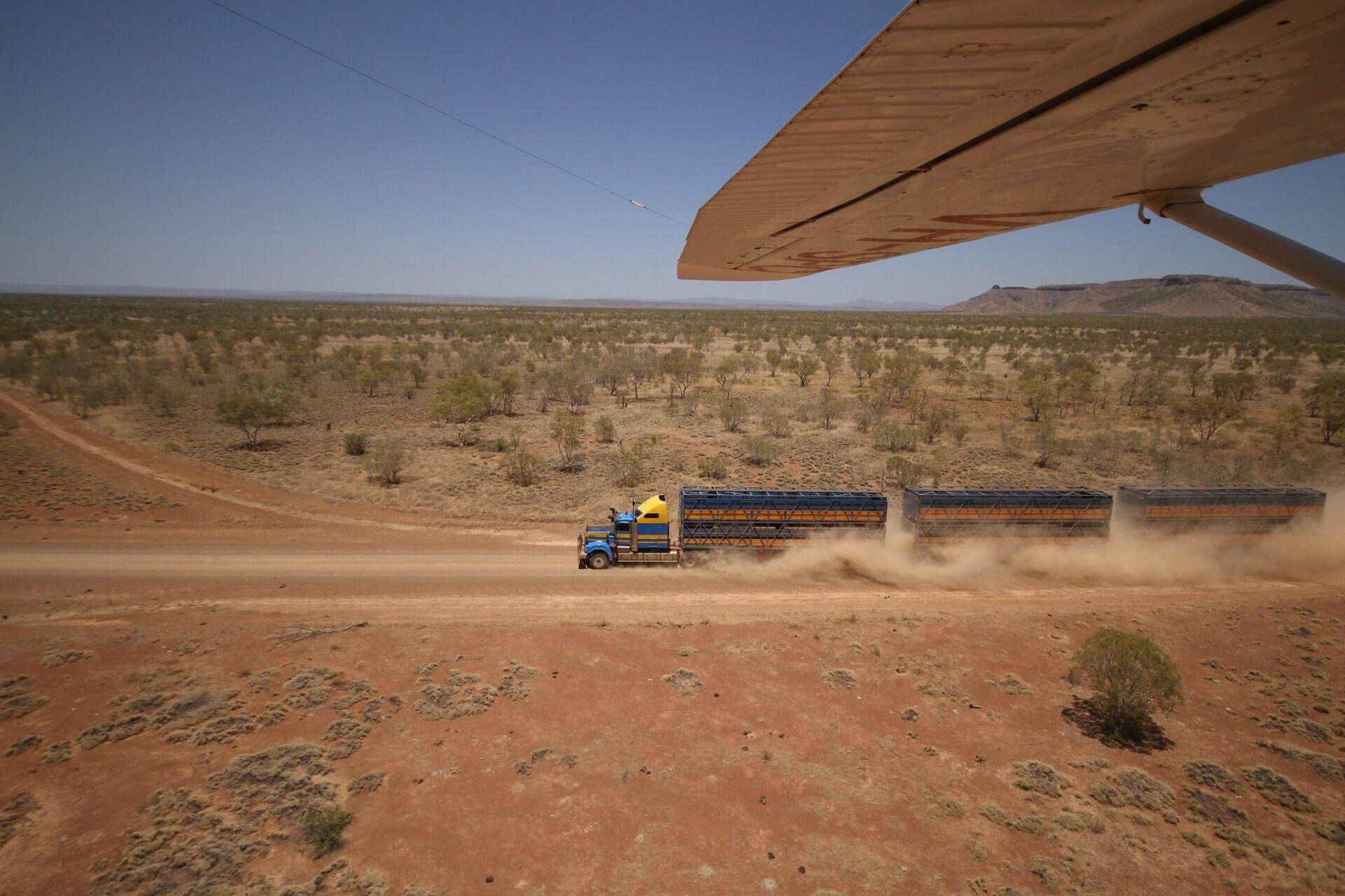 Truck hauling trailers on a dusty outback road, viewed from the wing of a plane.