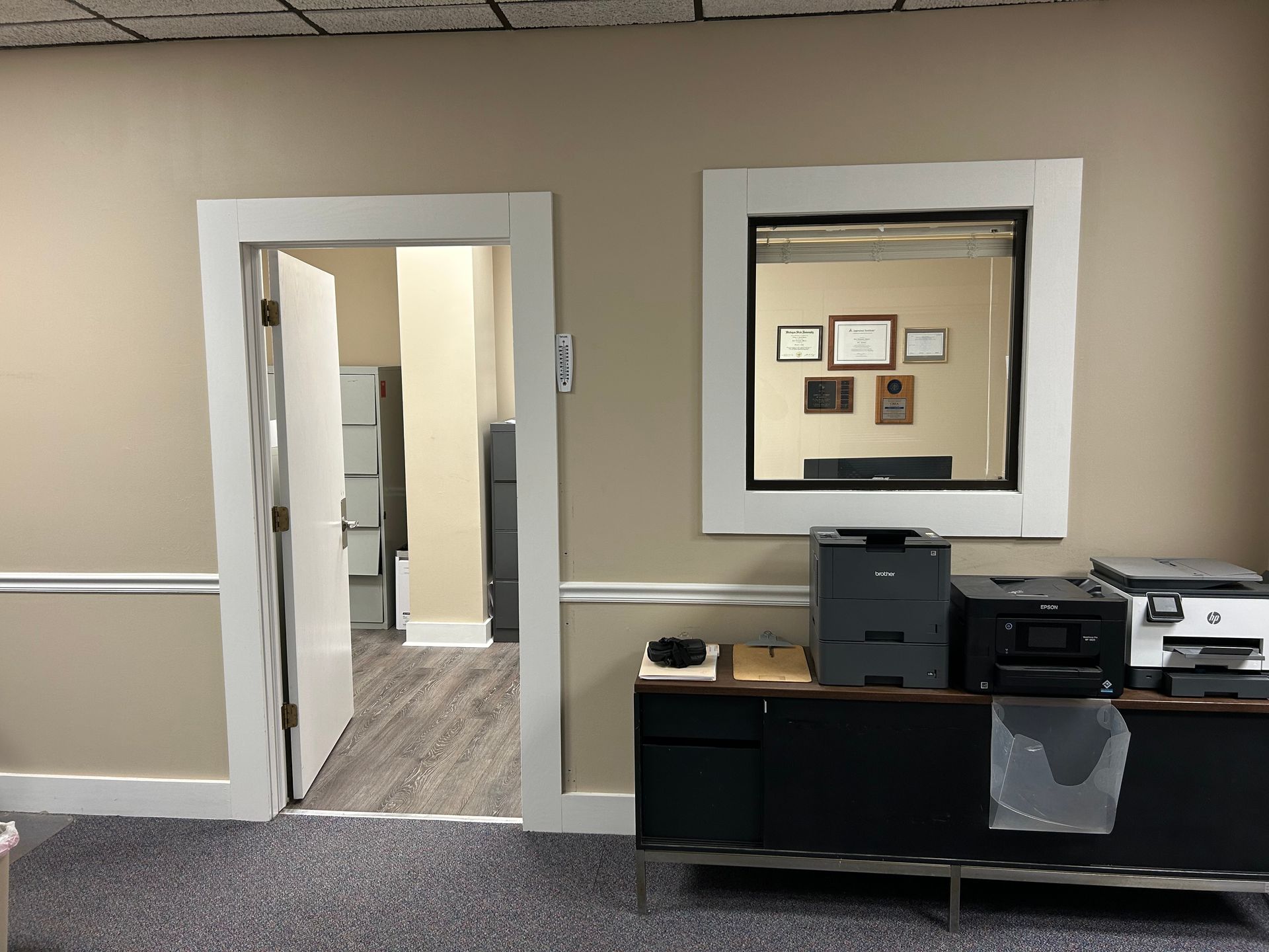 A room with a mirror on the wall and a desk with printers on it