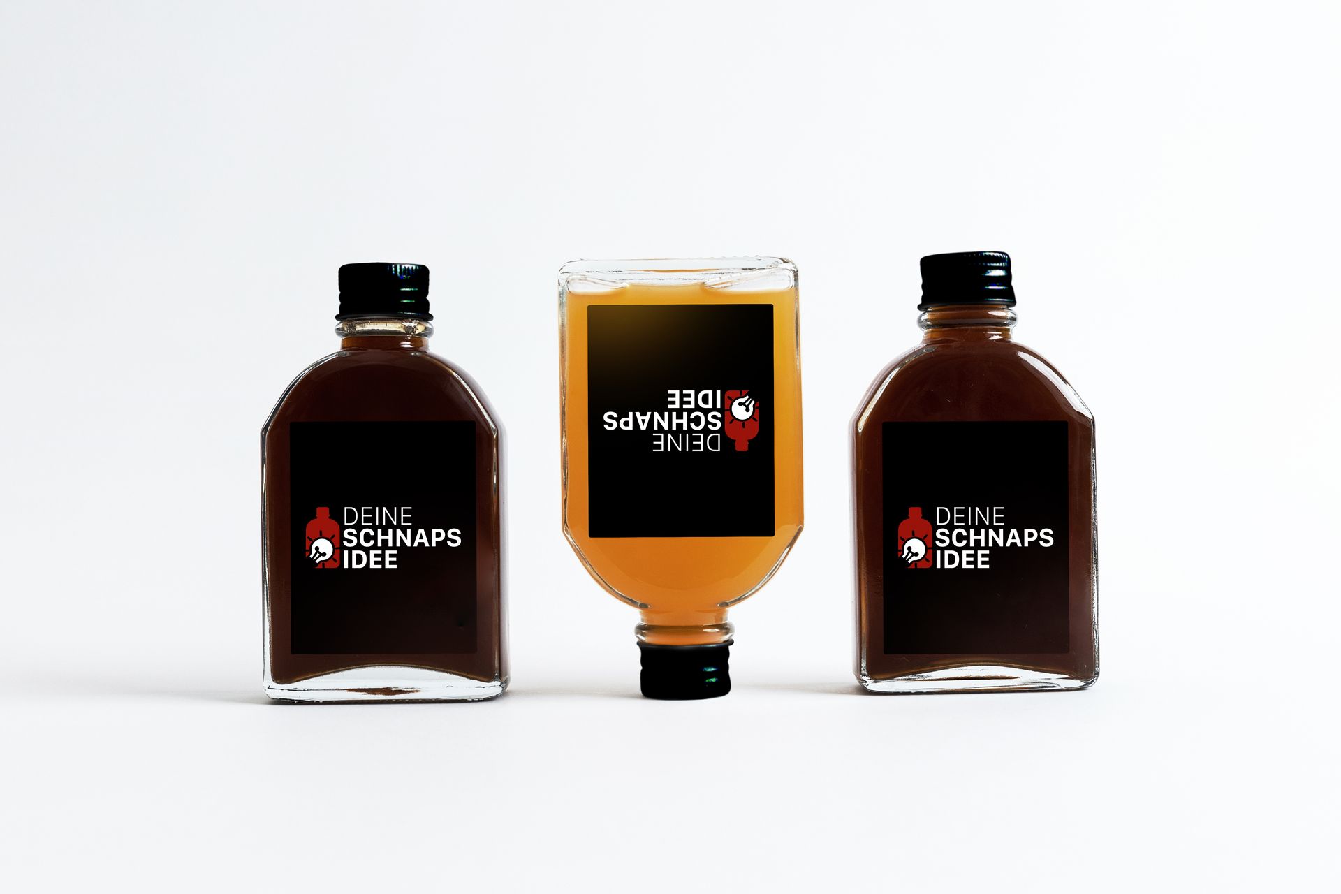 Drei kleine Flaschen Soße sind auf einer weißen Fläche aufgereiht.