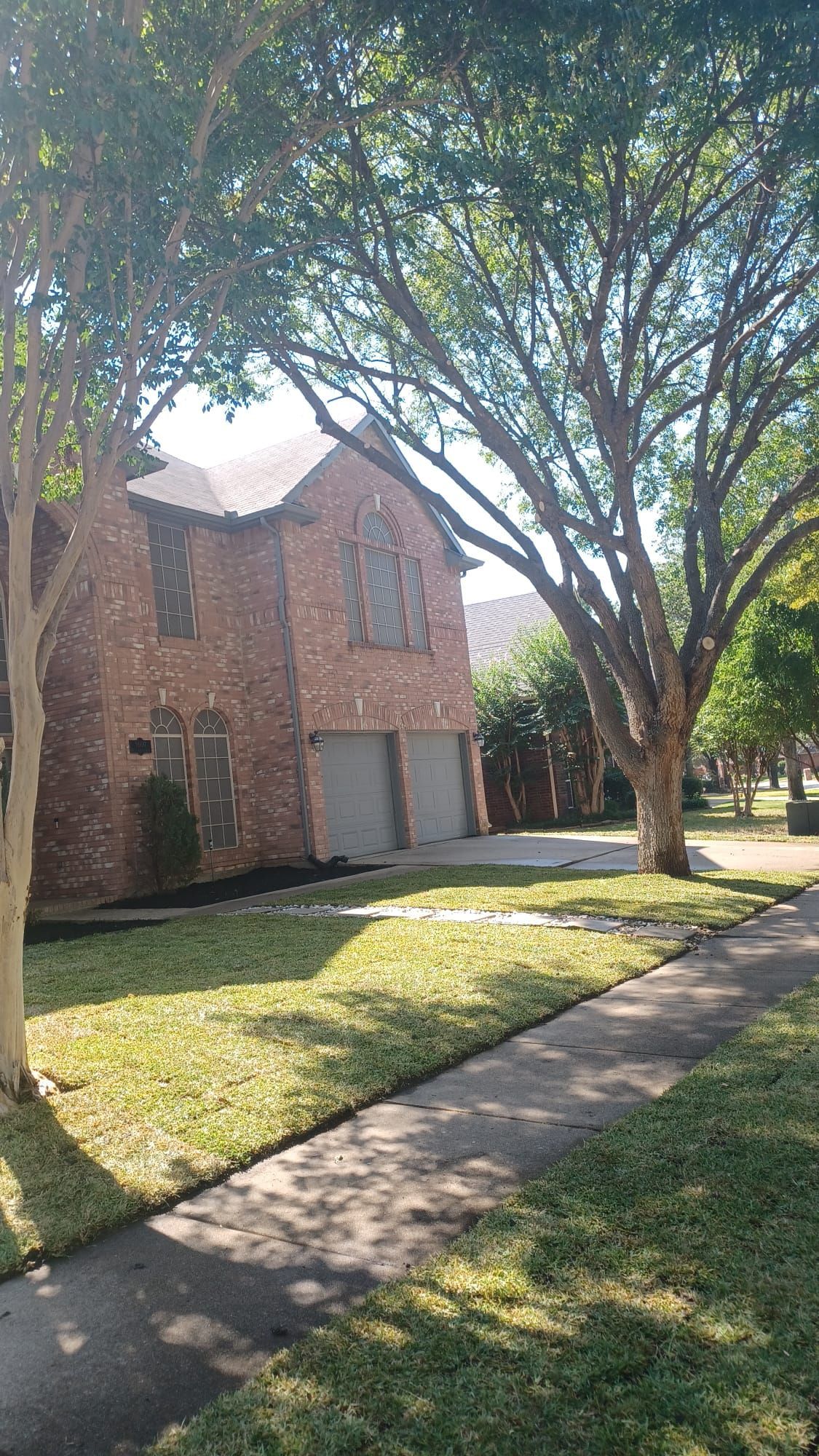 A large brick house with two garages and a tree in front of it.