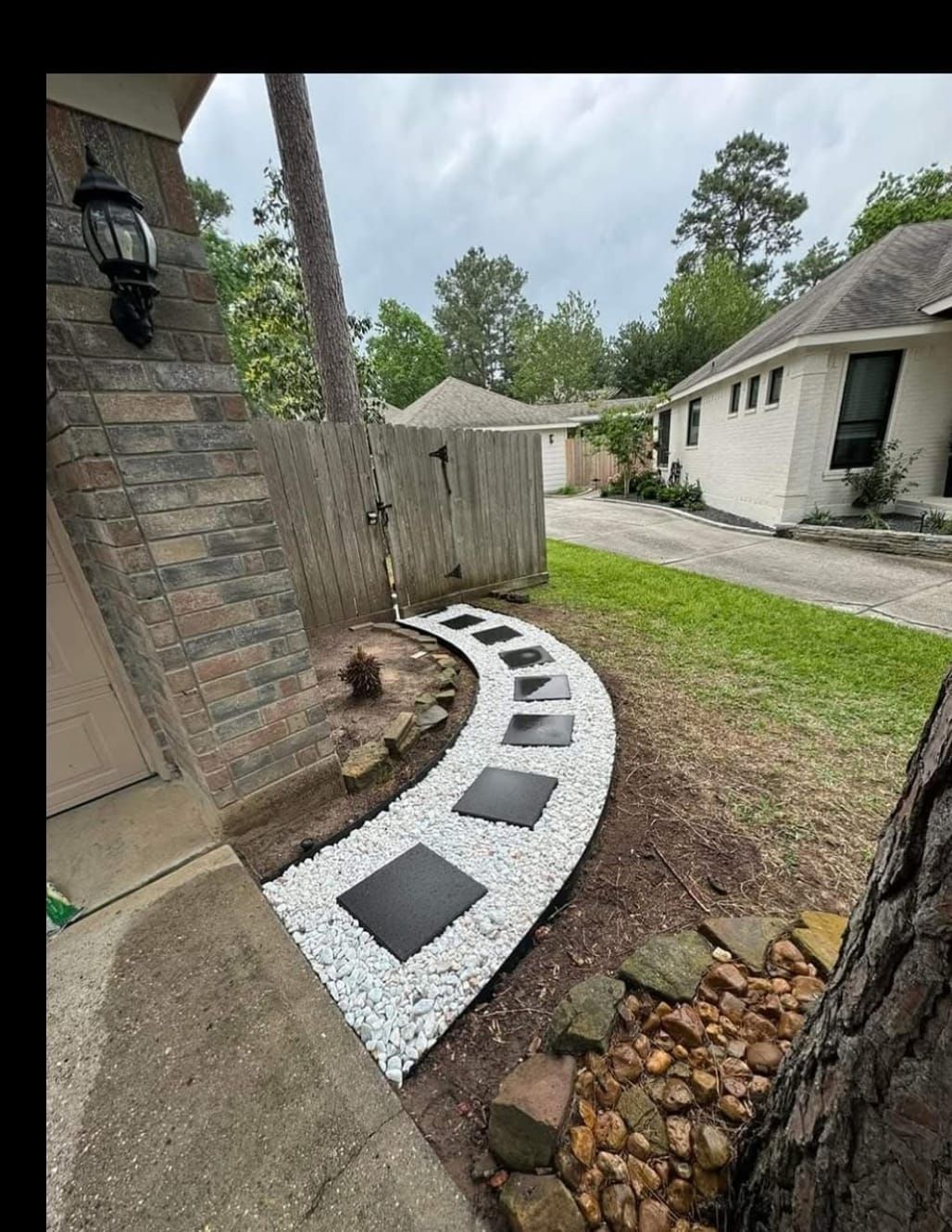 A walkway with white gravel and black squares in front of a house.