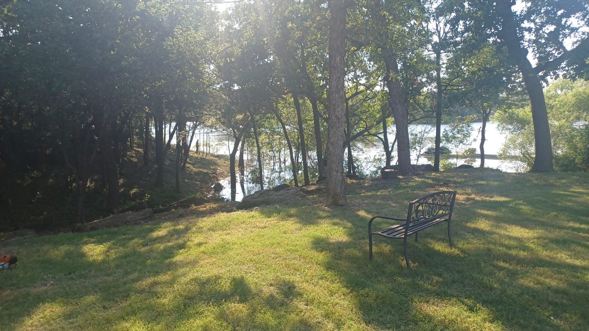 A park bench is sitting in the grass near a lake surrounded by trees.