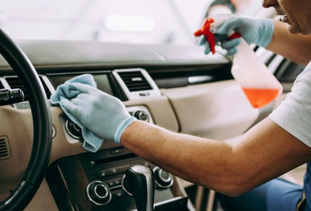Person cleaning a car dashboard with a spray bottle and cloth, wearing gloves.