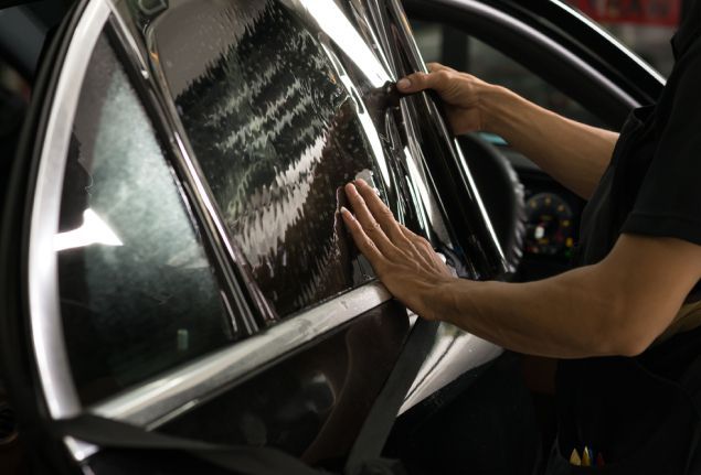Person applying window tint to a car window, inside a car, with hands smoothing the film.