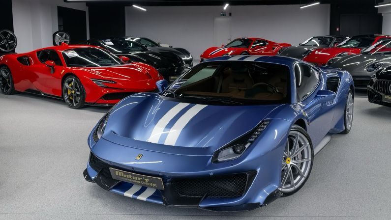 A blue ferrari 488 pista is parked in a showroom next to a red ferrari.