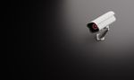 A security camera with a red light on it is sitting on a black surface.