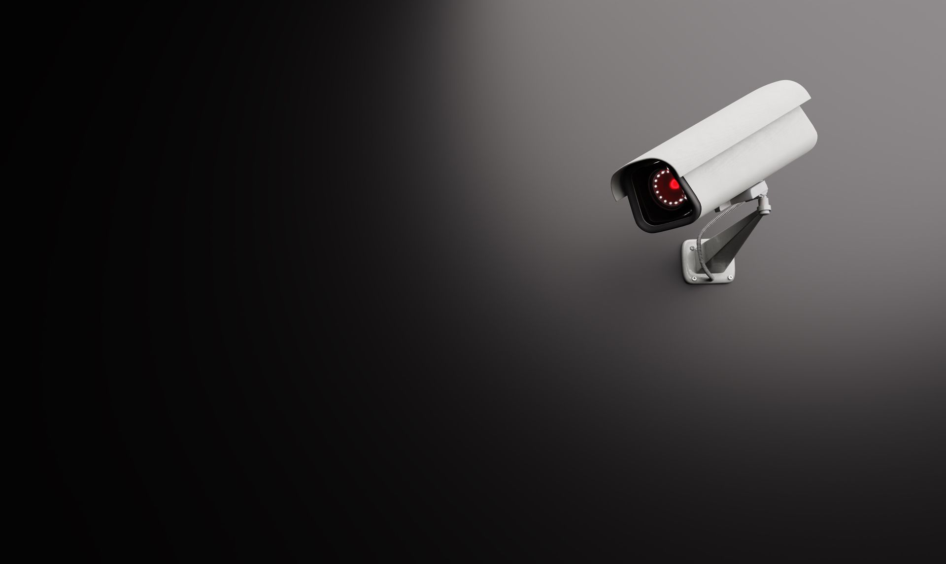 A security camera with a red light on it is sitting on a black surface.