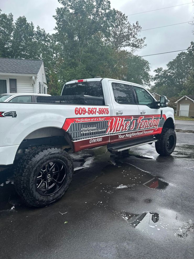 White truck with black wheels, branded with business name and phone number, parked on wet pavement.