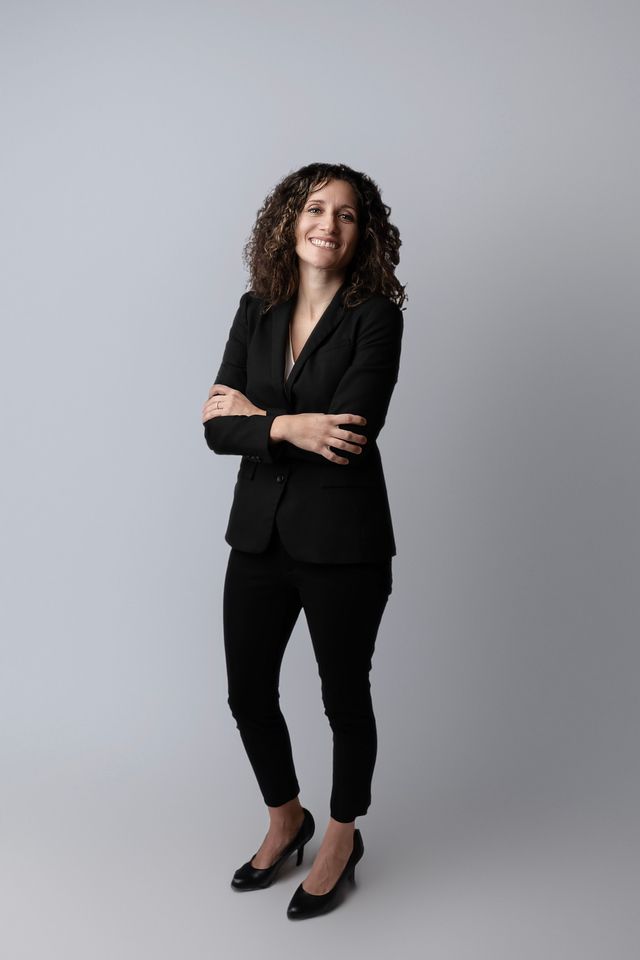 Woman in black suit, arms crossed, smiling.