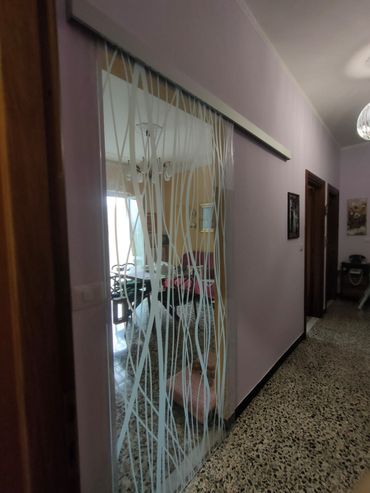 Una porta scorrevole in vetro con un motivo astratto bianco a forma di albero, installata in un corridoio con pareti color lilla chiaro.