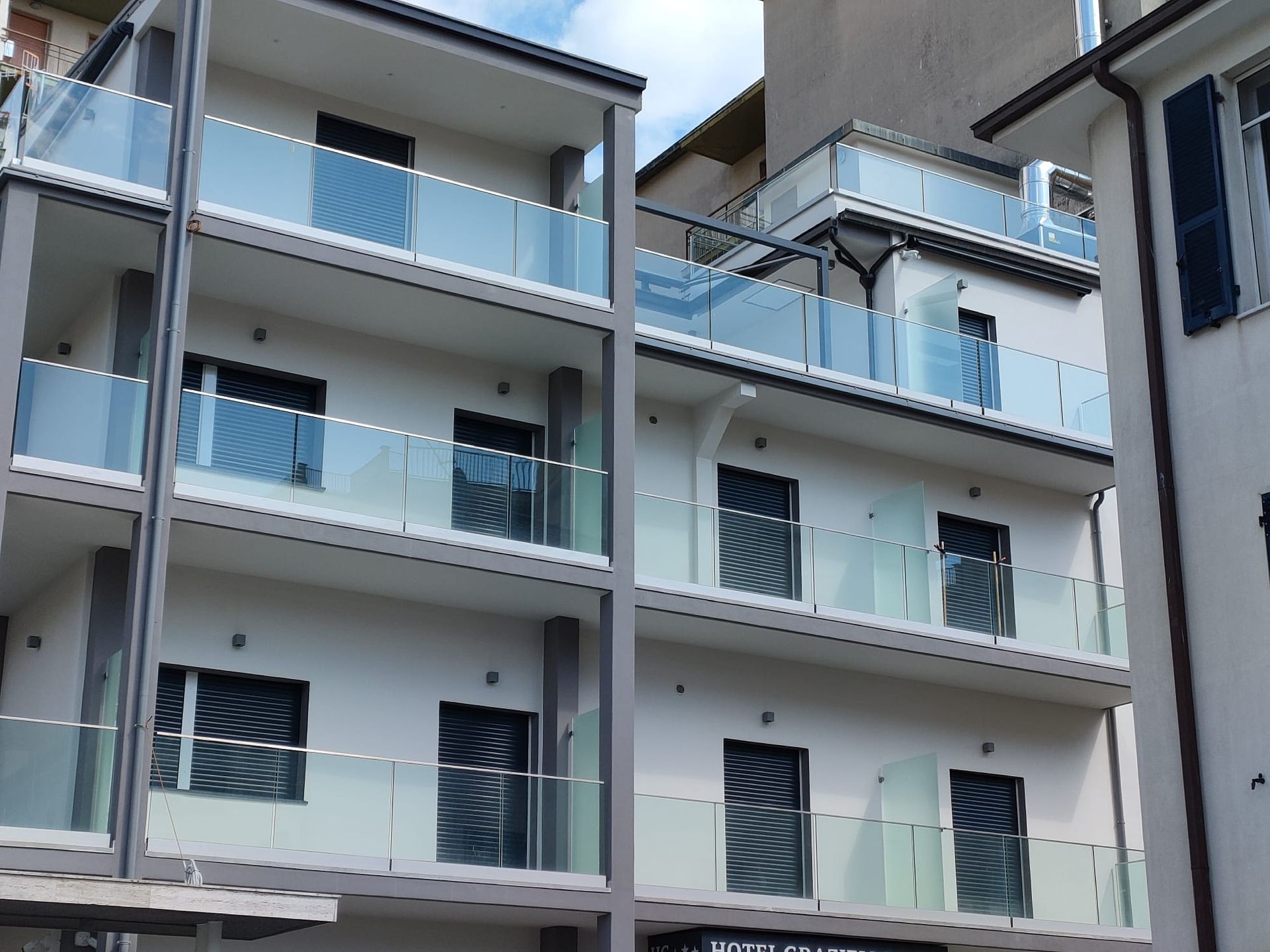 Un moderno edificio residenziale a più piani con pareti bianche, infissi neri e balconi con ringhiere in vetro.