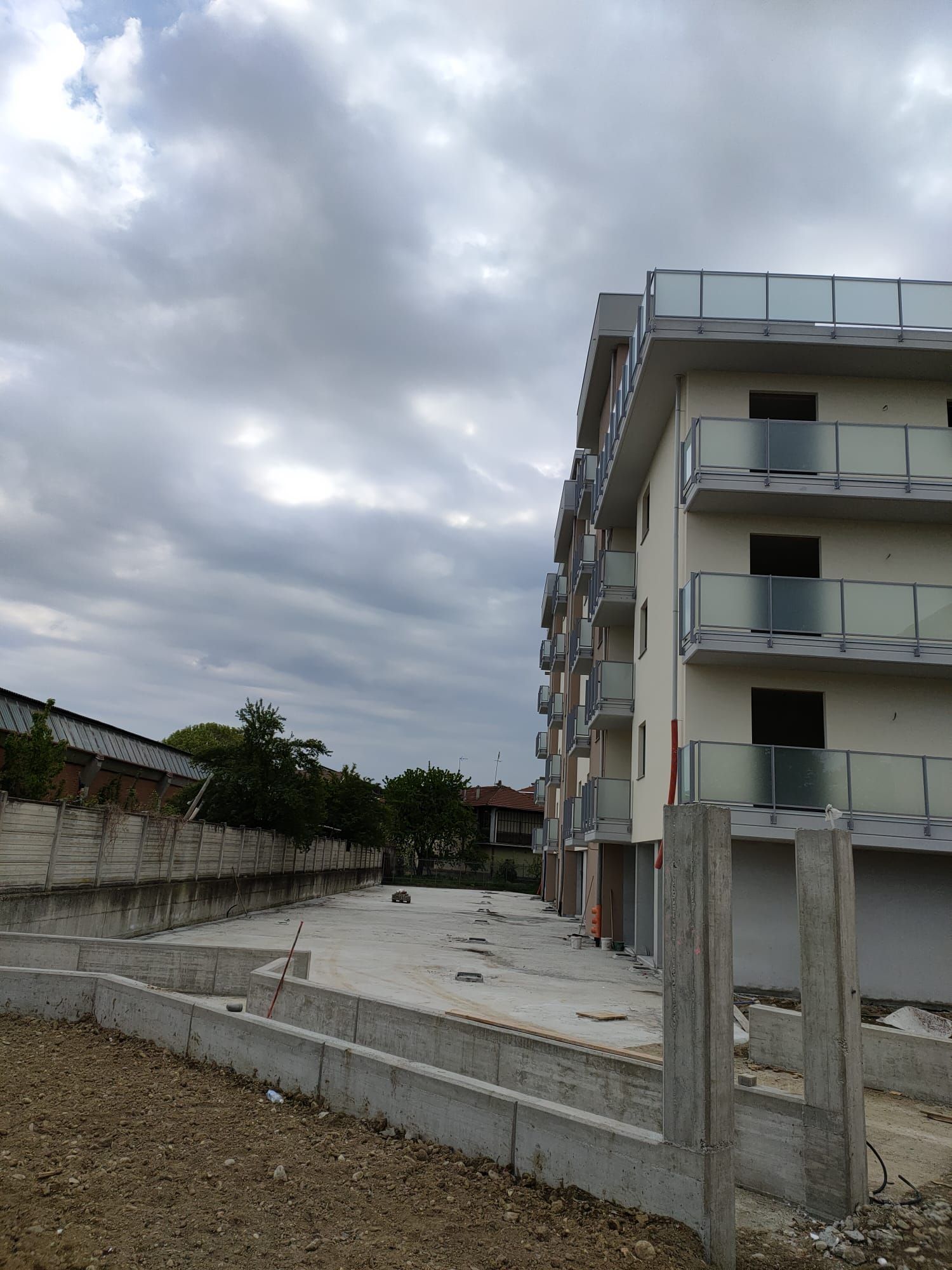 Un condominio a più piani con balconi si erge accanto a un cantiere vuoto e incompiuto, sotto un cielo nuvoloso.