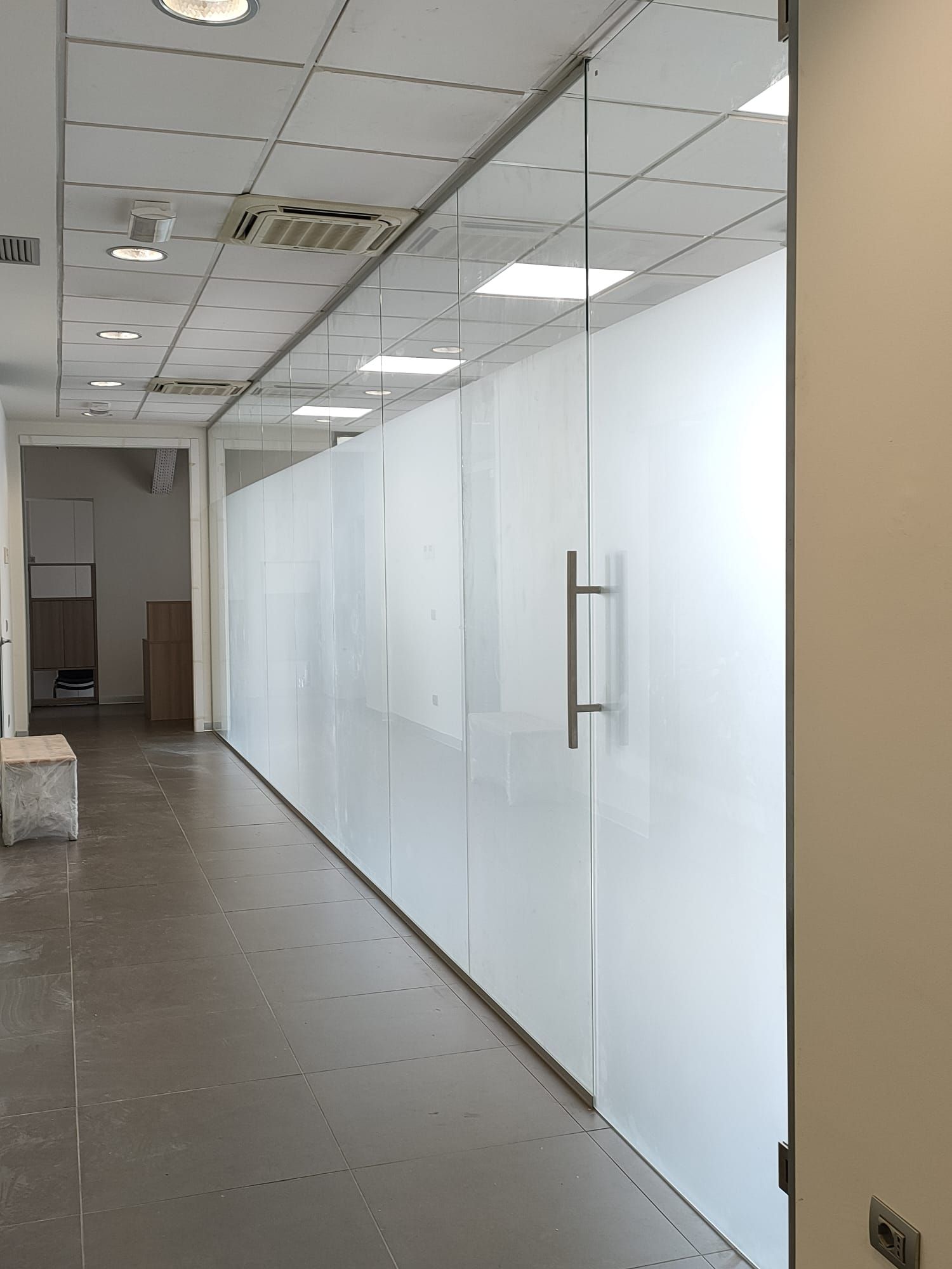 Un corridoio caratterizzato da una parete divisoria in vetro satinato a tutta altezza con maniglia in metallo e controsoffitto.