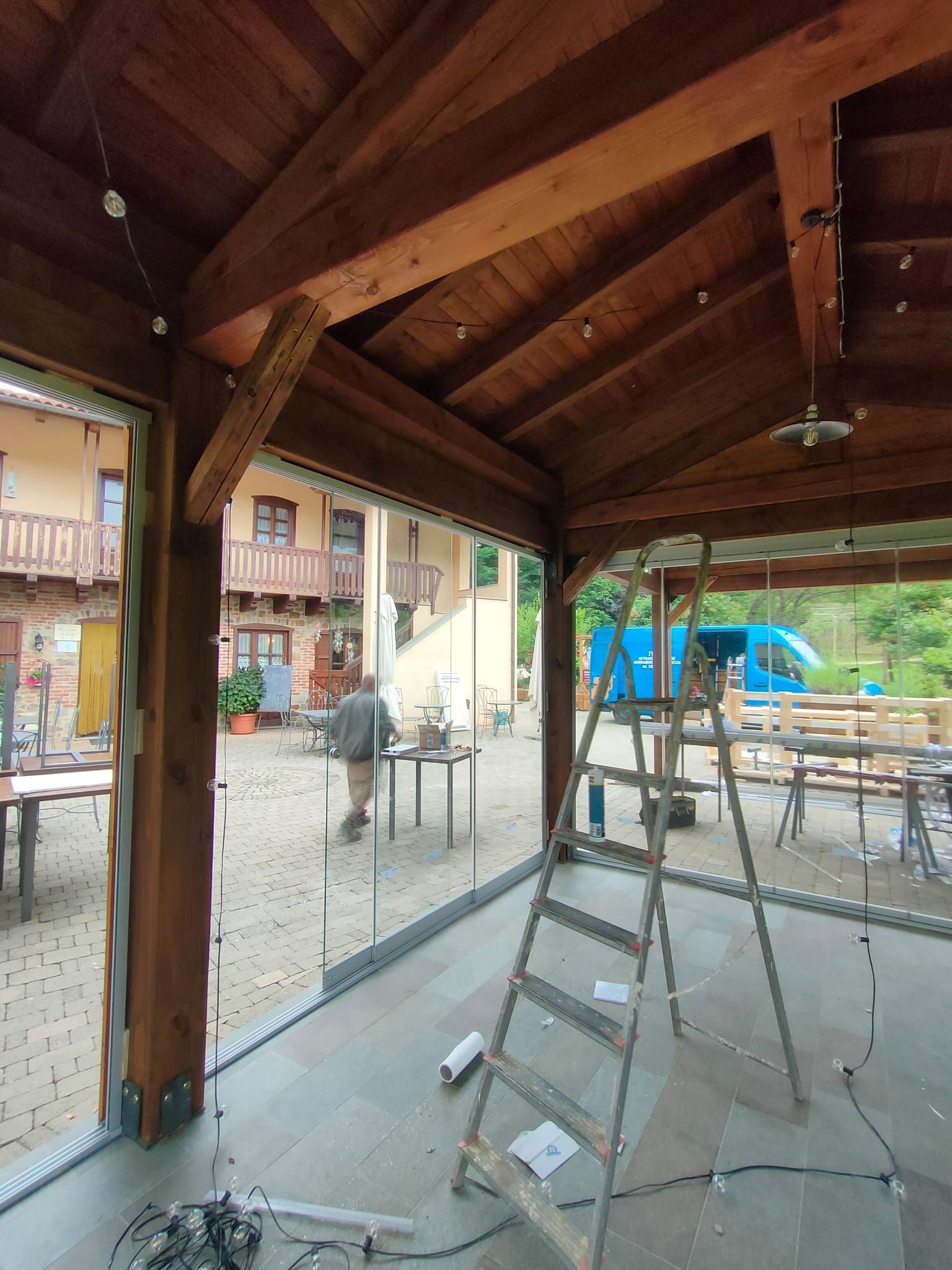 Una scala di metallo si erge sul patio all'interno di un gazebo in legno con porte scorrevoli in vetro, da cui si può scorgere il giardino sullo sfondo.