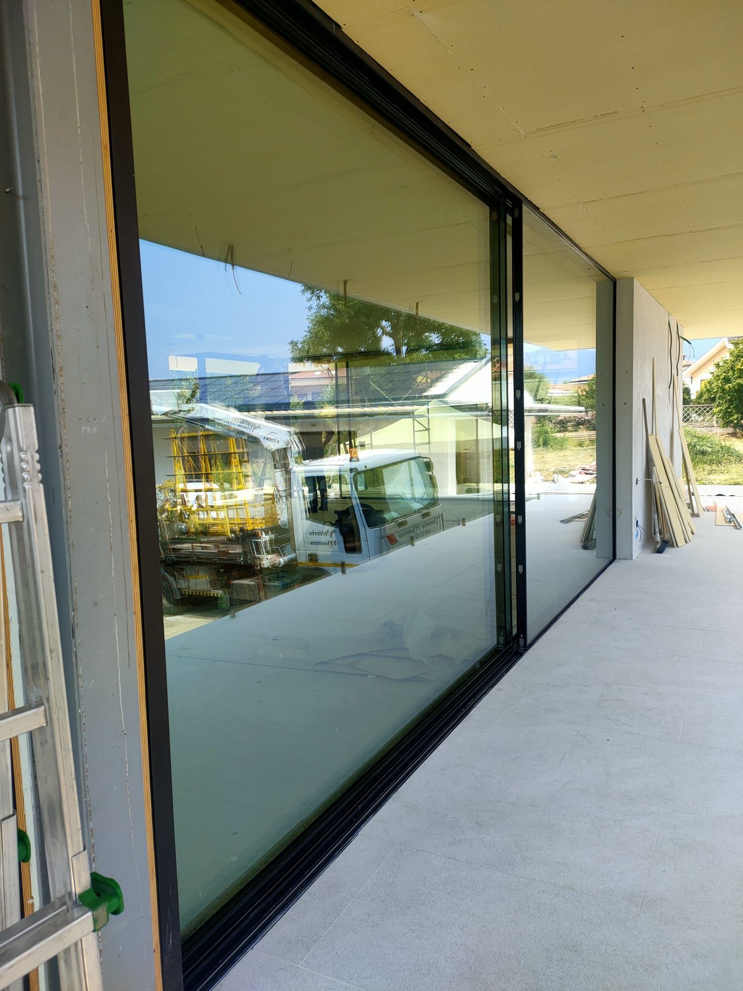 Ampie vetrate a tutta altezza con cornice nera, installate su un patio in cemento in un cantiere.