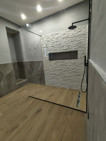 Bagno moderno con cabina doccia, pavimento piastrellato effetto legno, parete in pietra bianca con texture e rubinetteria nera.