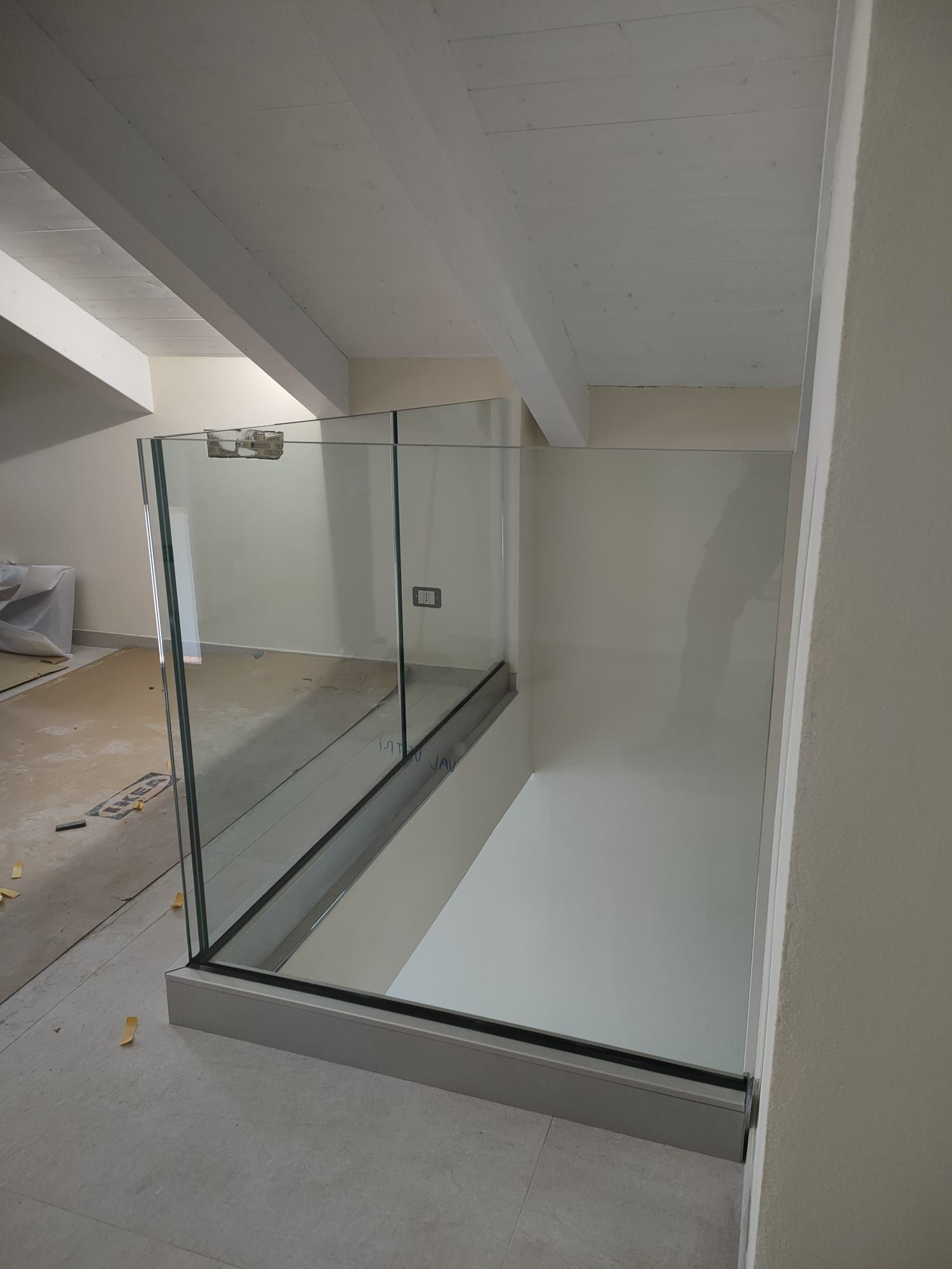 Box doccia in vetro con base grigia installato in una stanza con soffitto bianco inclinato.