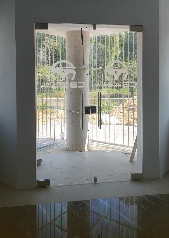 Una porta a vetri con il logo di un volante, incastonata in una semplice parete grigia, si affaccia su un'area recintata con alberi.