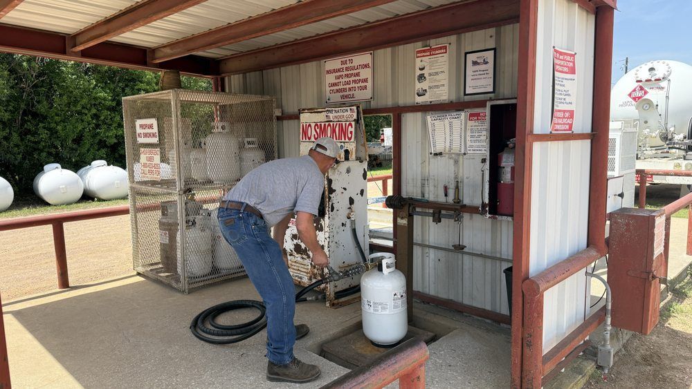 Man filling a propane tank at a filling station. White tanks, metal cage, and red and white signage are visible.
