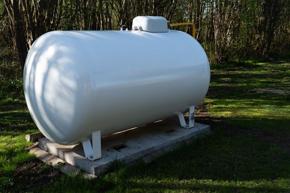 White propane tank on concrete base in grassy area.