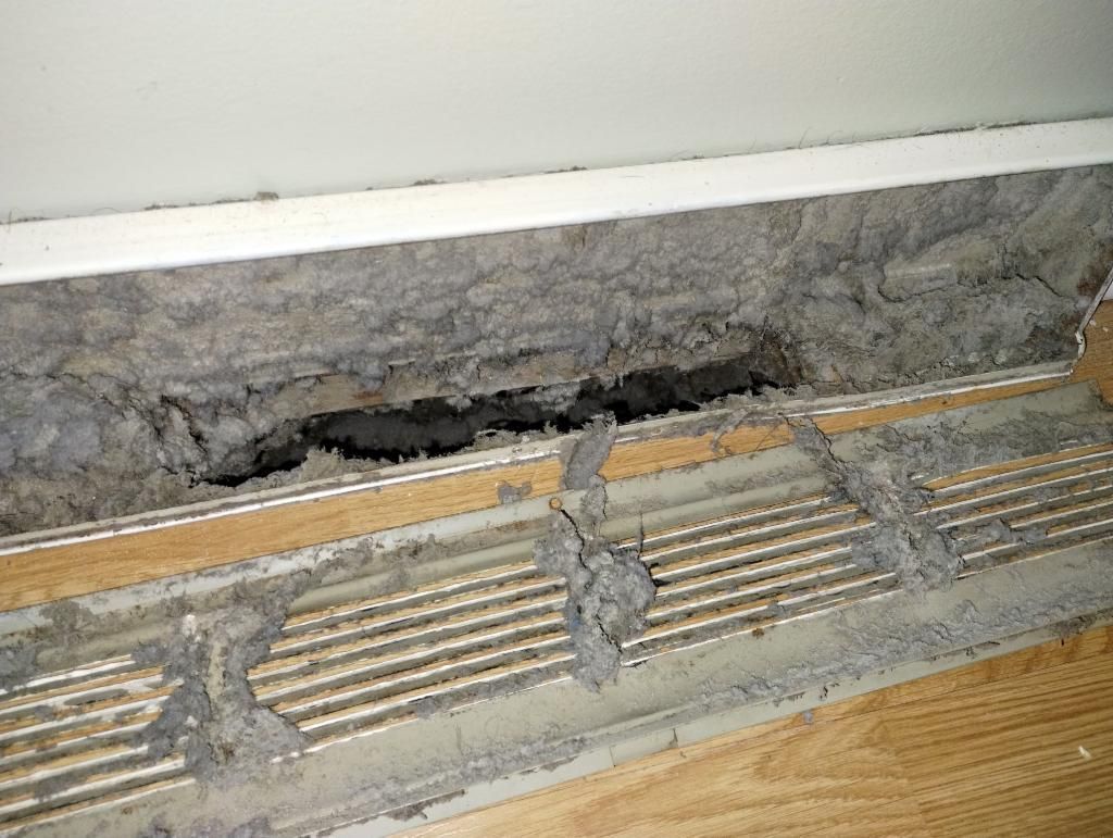 A close up of a dirty air vent on a wooden floor