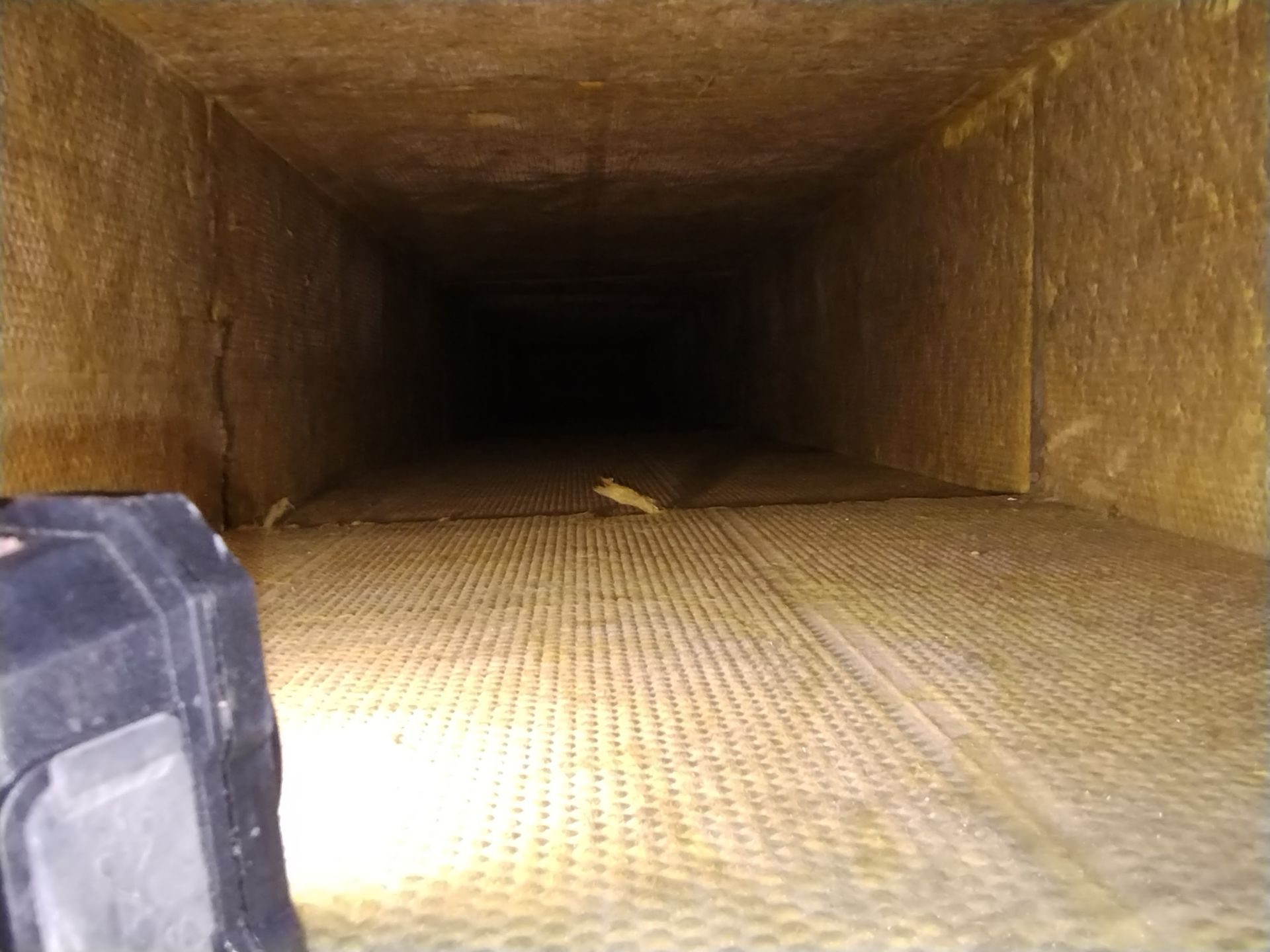 A person is looking down a duct with a flashlight