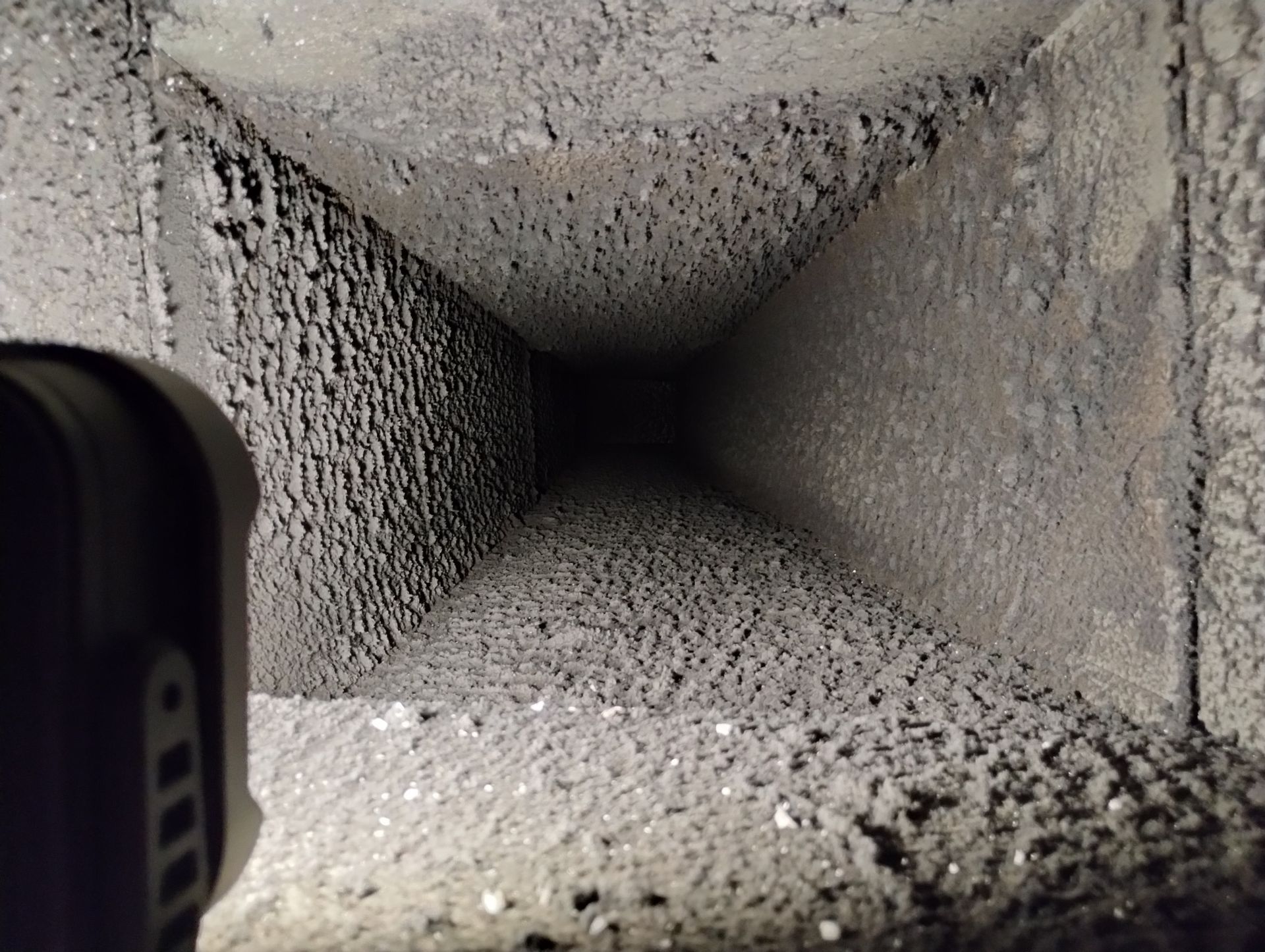 A person is taking a picture of a dirty duct with a flashlight