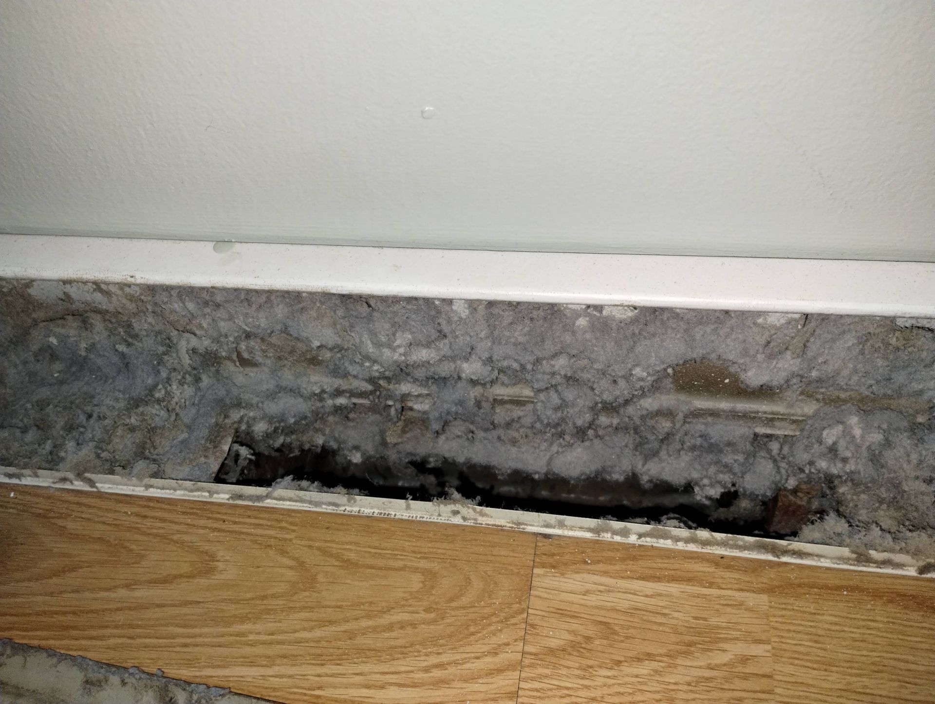 A close up of a hole in a wall next to a wooden floor