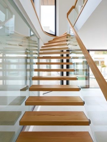 Wooden floating staircase with glass railing and natural light.
