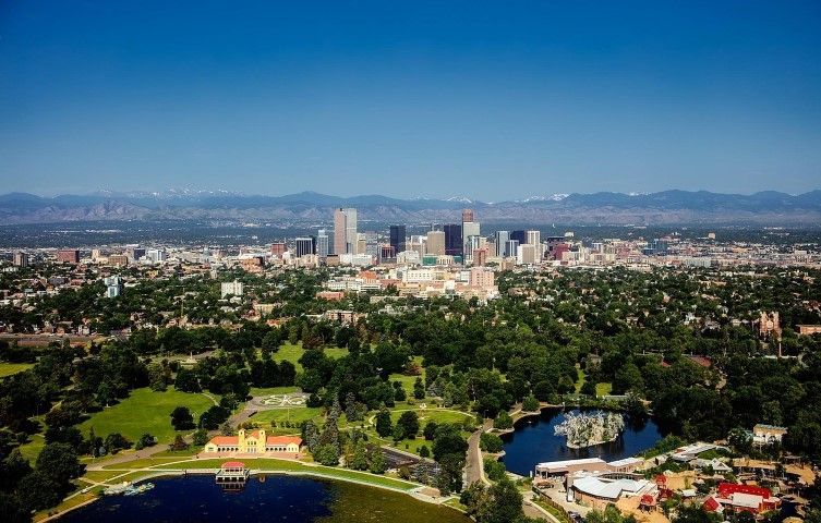 Aerial view of Colorado Springs with a park and downtown skyscrapers under a clear blue sky.