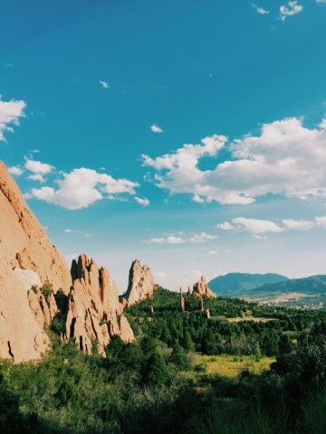 Red rock formations and green trees under a blue sky with white clouds.