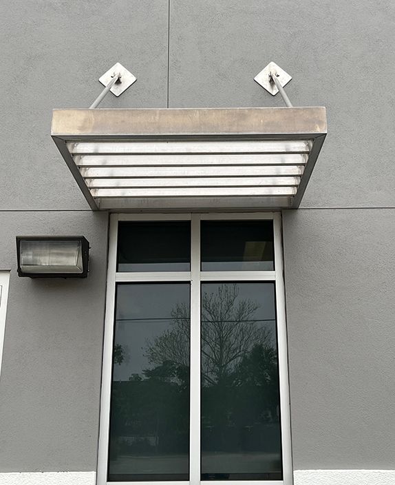 single slat awning mounted on stucco exterior by two metal poles and square plates