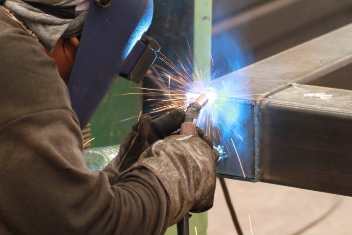 Welder wearing safety gear while welding steel pipes