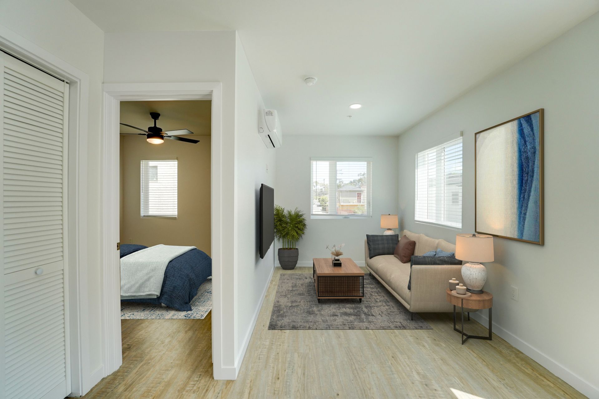 Interior view showing a living room with a beige sofa and a doorway leading to a bedroom with a bed and ceiling fan.