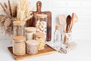 Glass storage jars containing grains and pasta, along with wooden utensils, arranged on a kitchen counter.