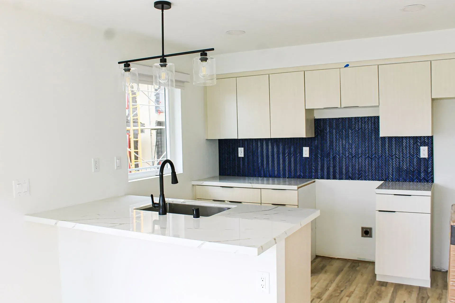 A kitchen with white cabinets, a white island with a sink, and a dark blue textured tile backsplash.