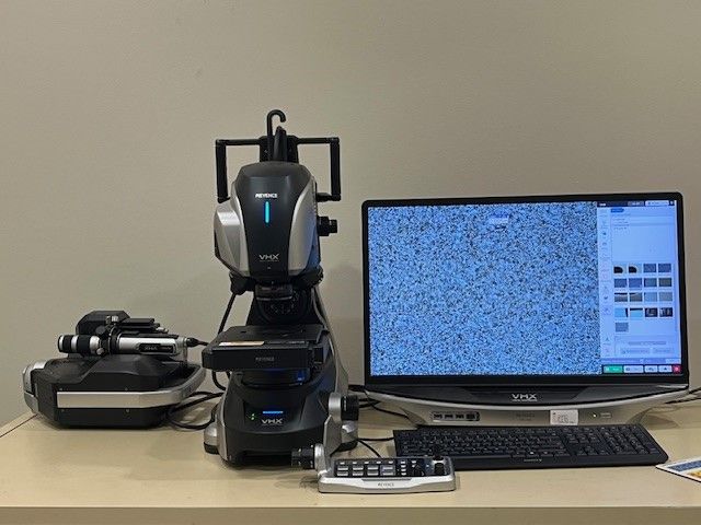 A microscope is sitting on a desk next to a computer monitor.