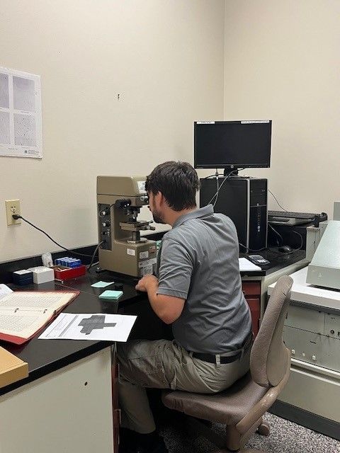 A man sits in front of a microscope in a lab