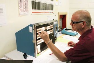 A man is sitting at a desk in front of a machine.