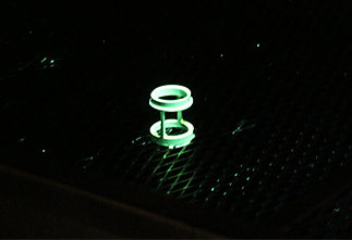 A green object is glowing in the dark on a black surface.