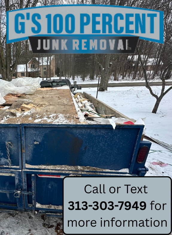 Black truck towing a blue trailer with logs on a snow-covered driveway, garage in the background.
